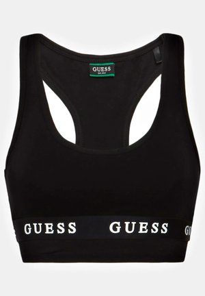 Brassière de sport noire dos nageur avec bande élastique portant le texte du logo GUESS en blanc et une étiquette de marque à l'intérieur du col.