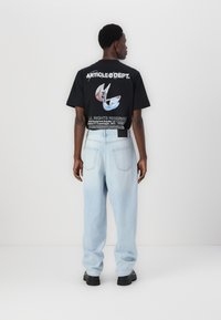 Black graphic t-shirt with a colorful design on the back, paired with light blue loose-fitting jeans and black chunky shoes.