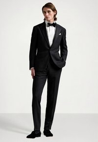 Μαύρο ταγιέρ με σατέν γιακά αιχμής, λευκό πουκάμισο και παπιγιόν. Στενή εφαρμογή με ομαλή υφή, σε συνδυασμό με μαύρα υποδήματα.