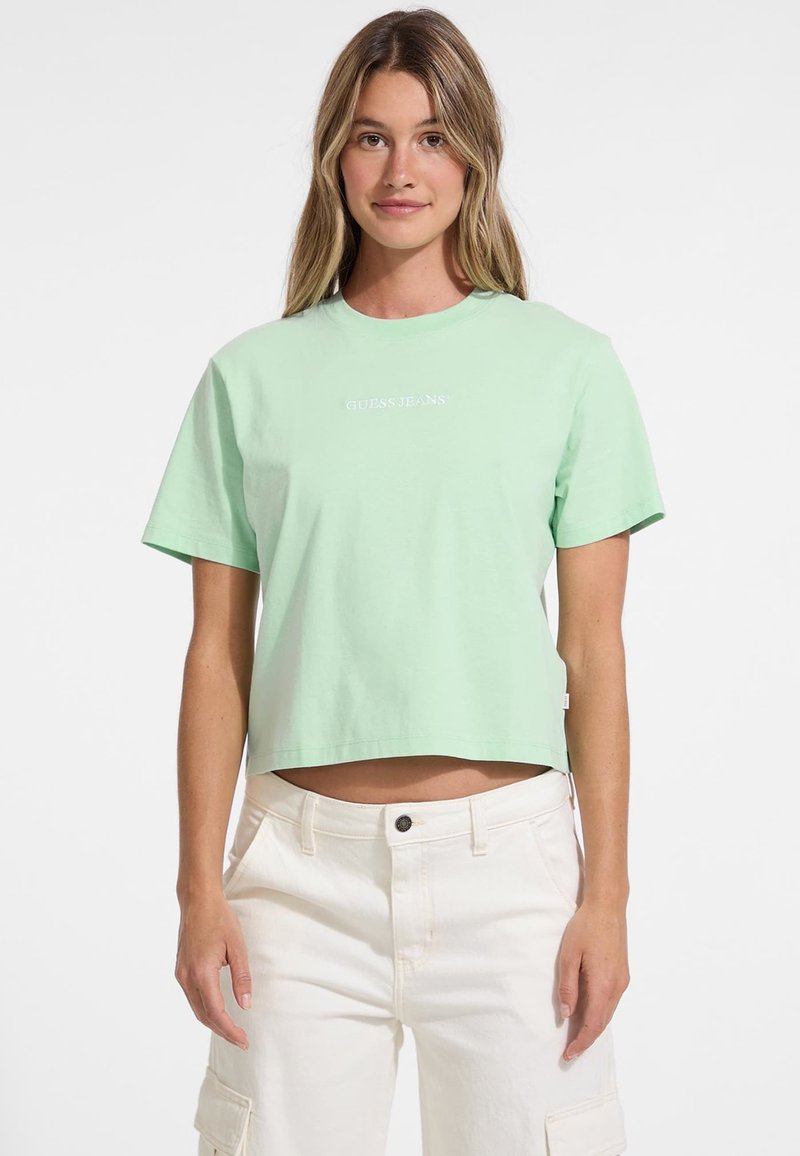 Minttu vihreä lyhythihainen cropped t-paita, valmistettu puuvillasta, jossa on pyöreä kaula-aukko ja valkoinen "GUESS. JEANS" -logo.