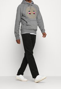 Felpa grigia con cappuccio a coulisse, logo e tasca a marsupio, abbinata a pantaloni in velluto a coste neri e sneaker bianche. Tessuto strutturato e vestibilità comoda.