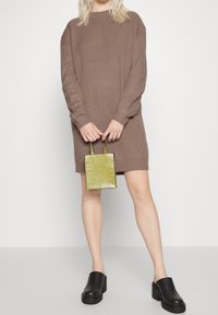 Abito maglione marrone a maniche lunghe, abbinato a una piccola borsa a tracolla verde con motivo coccodrillo e mule nere con plateau.