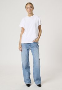 T-shirt bianca a maniche corte con una vestibilità rilassata, abbinata a jeans a gamba larga di colore azzurro chiaro. I jeans hanno una finitura sbiadita e una struttura dritta.
