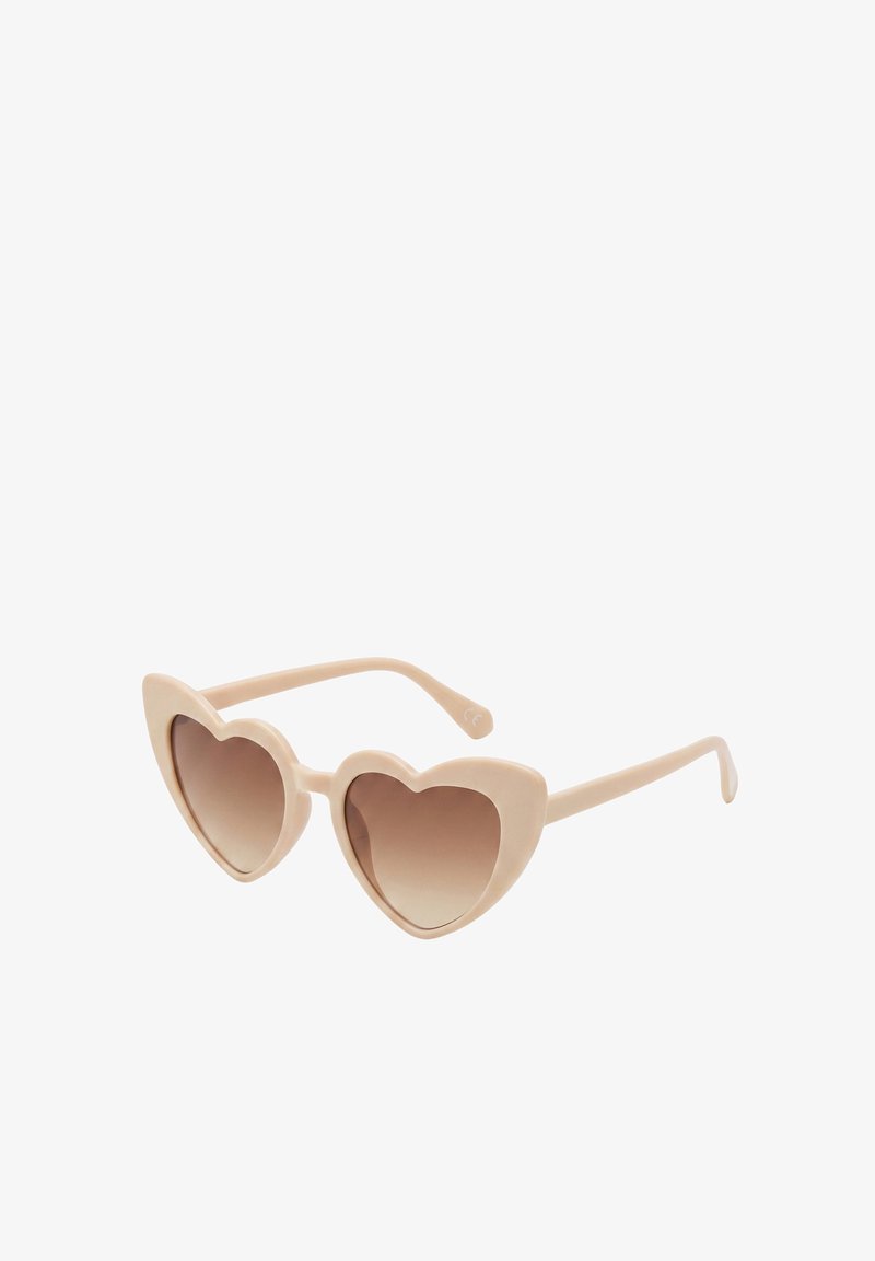 Lunettes de soleil beige en forme de cœur avec des verres marron dégradés et des branches fines, présentées sous un léger angle sur fond blanc.