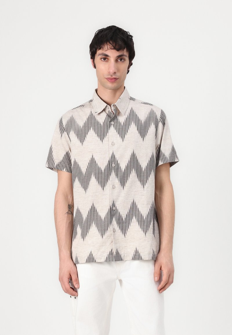 Camicia a maniche corte con bottoni di colore beige con motivo a zigzag nero. Presenta un colletto a punta e un tessuto leggero, adatta per un abbigliamento casual.