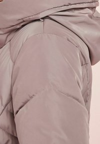 Close-up of a taupe padded jacket sleeve with visible seam details and a folded collar near the shoulder.