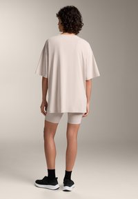 Bež oversized majica kratkih rukava, napravljena od mekog materijala. Uparena s kratkim biciklističkim hlačama svijetle boje i crnim sportskim cipelama.