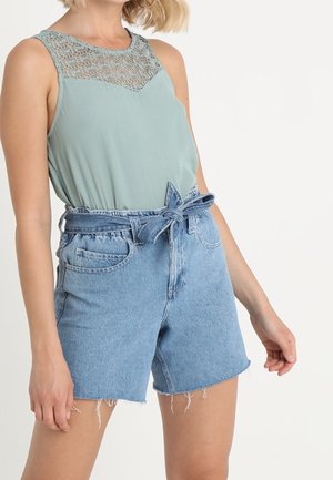 Top senza maniche verde chiaro con dettagli in pizzo sul collo, abbinato a pantaloni shorts in denim blu a vita alta con vita con cintura e orlo sfrangiato.