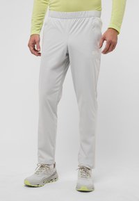 Helle graue Sweatpants mit elastischem Bund, glatter Textur und Seitentaschen. Kombiniert mit grauen und gelben Sportschuhen.