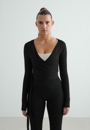 Top nero a maniche lunghe avvolgente con scollo a V profondo, abbinato a leggings neri a vita alta. Tessuto morbido, design aderente e dettaglio con legatura laterale.