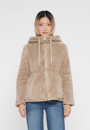 Tan färgad faux fur zip-up jacka med huva, som har två frontfickor och beige dragkedjor. Mjuk textur med en avslappnad passform.