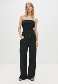 Top in denim nero senza spalline con righe verticali, abbinato a jeans neri a vita alta e a gamba larga. Presenta tasche frontali e dettagli di cucitura sottili.