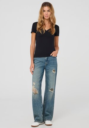 T-shirt nera con scollo a V abbinata a jeans a gamba larga blu sbiaditi con grandi strappi, zone usurate, e sneakers bianche per un look informale.