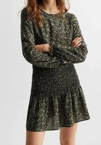 Black and green floral dress with long sleeves, smocked bodice, and flared skirt. Made of lightweight fabric with a soft texture.