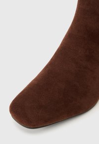 Botte ankle en suède marron avec un bout carré et une texture lisse. Présente un design effilé et une semelle fine, adaptée à diverses tenues.