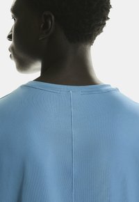 Chemise à manches courtes bleu clair, texture lisse, col rond, dotée d'une couture centrale au dos, fabriquée en tissu respirant.
