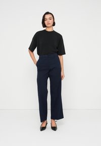 Μαύρο φαρδύ μπλουζάκι συνδυασμένο με ναυτικό, ψηλόμεσο παντελόνι με φαρδιά μπατζάκια και μαύρες μπαλαρίνες με μυτερή μύτη πάνω σε απλό λευκό φόντο.