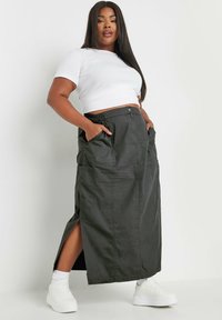 Tummanvihreä maksimekko, jossa on sivutaskut, kaksi etutaskua, joustava vyötärö ja yhdistetty valkoisen lyhyen topin sekä valkoisten lenkkarien kanssa.