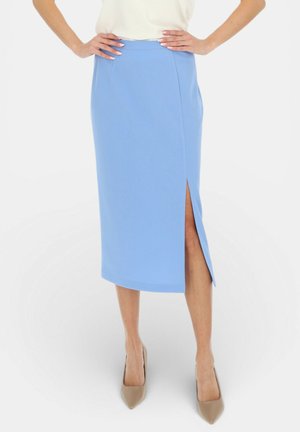 Kobieta nosząca jasnoniebieską midi spódnicę z przednim rozcięciem, w połączeniu z beżowymi szpilkami z ostrym noskiem i białą koszulką wpuszczoną w spódnicę.