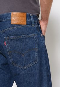 Blaue Jeans aus Denim mit geradem Schnitt, ausgestattet mit einem braunen Leder-Logo-Patch und kontrastierenden gelben Nähten. Beinhaltet hintere Taschen mit Nahtdetails.