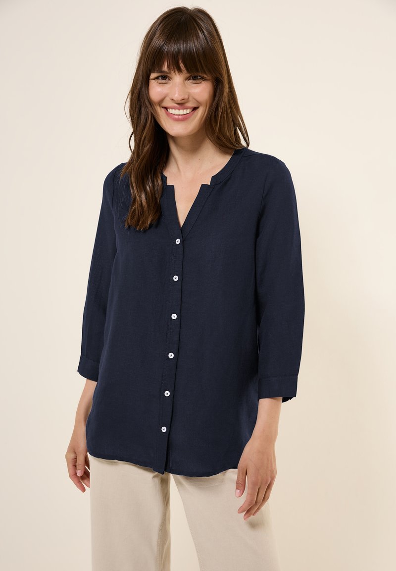 Camicia di lino blu navy con scollo a V, chiusura a bottoni e maniche a tre quarti, caratterizzata da un orlo dritto e una texture sottile.