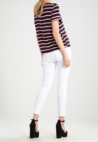Top de rayas en azul marino y rojo de manga corta combinado con pantalones skinny blancos y tacones de plataforma negros, mostrando una combinación de atuendo casual.
