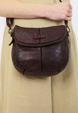 Brown leather crossbody bag with a rounded shape, zip closure, and a leather tag. Smooth texture with subtle shine; adjustable strap attached.