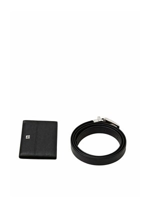 Portafoglio in pelle nera con un piccolo logo e una cintura in pelle nera arrotolata con fibbia in metallo argentato su sfondo bianco.