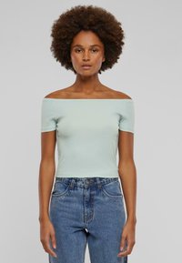 Lyseblå off-shoulder topp laget av myk bomull. Korte ermer, tettsittende design, kombinert med høytlivde blå jeans.