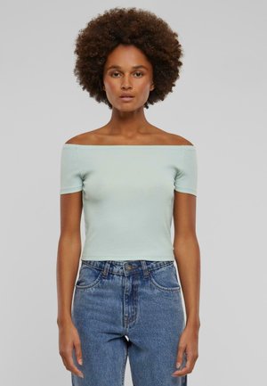 Lyseblå off-shoulder topp laget av myk bomull. Korte ermer, tettsittende design, kombinert med høytlivde blå jeans.