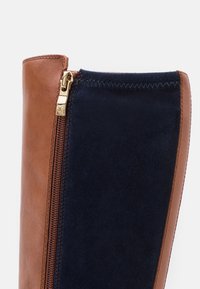 Brown leather and navy suede boot featuring a side zipper, contrasting textures, and precise stitching along the edges.