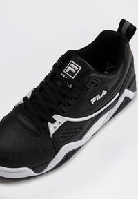 Baskets FILA noir et blanc avec lacets noirs, col rembourré, bout perforé et logo sur la languette et le côté, en angle sur fond blanc.