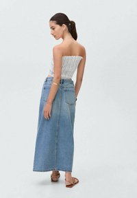 Denim maksi krilo v svetlo modri barvi z visokim pasom, ki vključuje dva zadnja žepa in ravno silhueto. Parjeno z belim, prugastim crop topom.