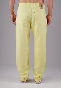 Light yellow denim pants with a relaxed fit, featuring two back pockets and a branded leather patch on the waistband.