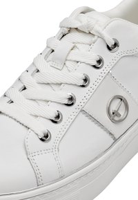 Sneaker blanc avec tige en cuir lisse, lacets en coton plats, œillets argentés et accent logo circulaire sur le côté. Semelle en caoutchouc plate.