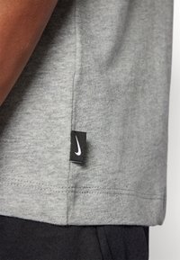 Siva pamučna majica s crnim Nike logotipom na rubu. Ima kratke rukave i glatku teksturu. Donji rub je prošiven.