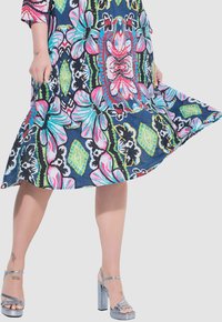 Vestido colorido con un estampado floral que presenta diseños en rosa, azul y verde sobre un fondo azul marino. Acompañado de sandalias de tacón alto plateadas.