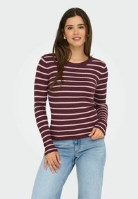 Pull à manches longues à côtes de couleur bordeaux profond avec des rayures horizontales roses. Encolure ras du cou, design ajusté, associé à un jean bleu clair.