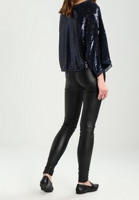 Laivastonsininen paljettipaita leveillä hihoilla yhdistettynä mustiin nahkajäljitelmäleggingsseihin ja mustiin balettitossuihin, joissa on sileä, kiiltävä pinta.