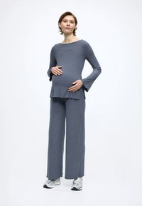 Szürke bordázott kismama felső, bővülő ujjakkal és peplum kialakítással, hozzáillő, széles szárú nadrággal párosítva. Az anyag puha és rugalmas hatású.