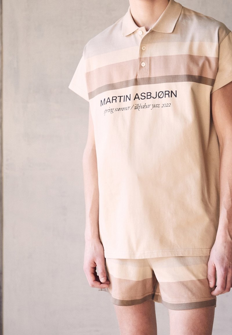 Polo à manches courtes et shorts assortis en beige avec des rayures discrètes. Doté d'un col et d'une marque sur le devant. Fabriqué en tissu doux.