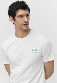 Hvid bomulds T-shirt med rund halsudskæring, korte ærmer og grøn tryk med teksten "1971 DOBBER SINCE 1971" på venstre bryst.