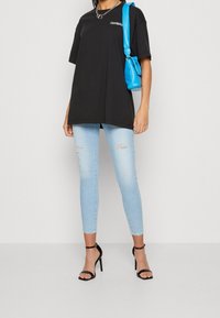 Camiseta negra oversize, vaqueros pitillo desgastados en azul claro, tacones negros con tiras y un bolso azul brillante. Textura suave, look casual.