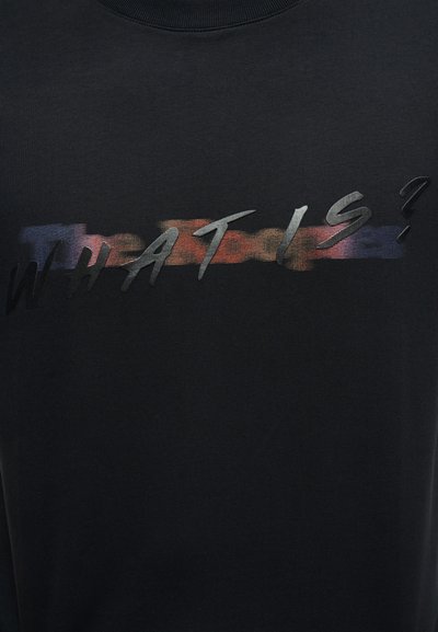 Μαύρο ύφασμα με τη λέξη "ΤΙ ΕΙΝΑΙ;" σε ανάγλυφα μαύρα γράμματα πάνω από μια θολή οριζόντια λωρίδα κόκκινων, πορτοκαλί και μπλε χρωμάτων.