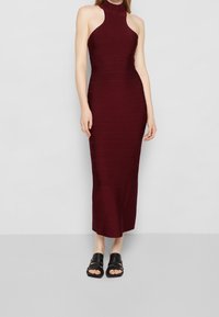 Bordové šaty na ramínka s přiléhavým korzetem a délkou do poloviny lýtek, s vroubkovanou texturou. V kombinaci s černými sandály na tenké řemínky.