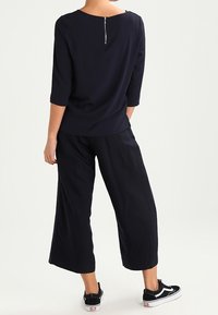 Top blu navy con maniche a tre quarti, presenta un dettaglio con zip sul retro, abbinato a culottes blu navy a vestibilità ampia e sneaker nere.