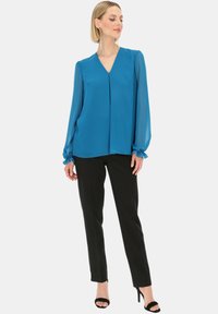 Błękitna bluzka z dekoltem w kształcie litery V z długimi, marszczonymi rękawami, zestawiona z czarnymi, dopasowanymi spodniami. Bluzka ma gładką, lekko spływającą fakturę i luźny krój.