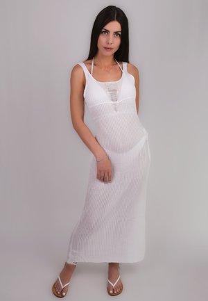 Abito lungo bianco a maglia con corpino aderente, schiena scoperta e righe verticali. Abbinato a infradito bianche e bracciale argento.