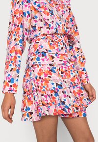 Vestido com padrão floral e camadas com franzidos, apresentando tons de rosa, laranja, azul e castanho. Feito de um tecido leve com cintura elástica.