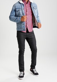 Dżinsowa kurtka z białym sztucznym futrem przy kołnierzu, czerwona i niebieska koszula w kratkę, czarne slim-fit spodnie i czarne sneakersy z białymi akcentami.